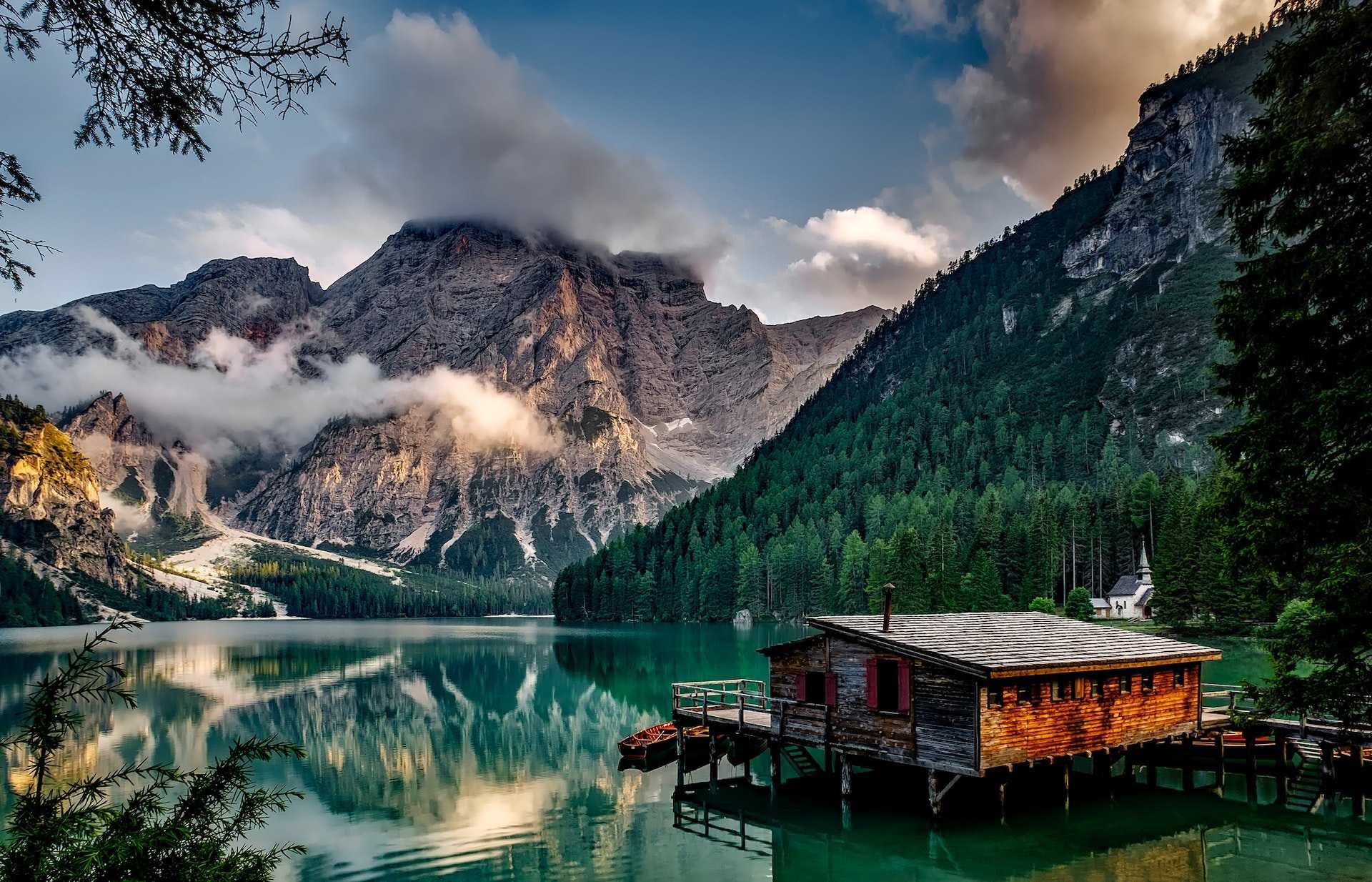 Mirror lake refelcting wooden house in middle of lake overlooking mountain ranges